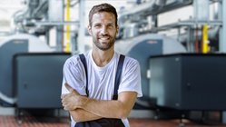 Ein lächelnder Mann in Arbeitskleidung mit verschänkten Armen