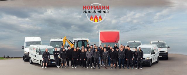 Eine Gruppe von Mitarbeitern steht stolz vor einer Reihe von Firmenfahrzeugen, die für Haustechnik-Dienstleistungen genutzt werden.